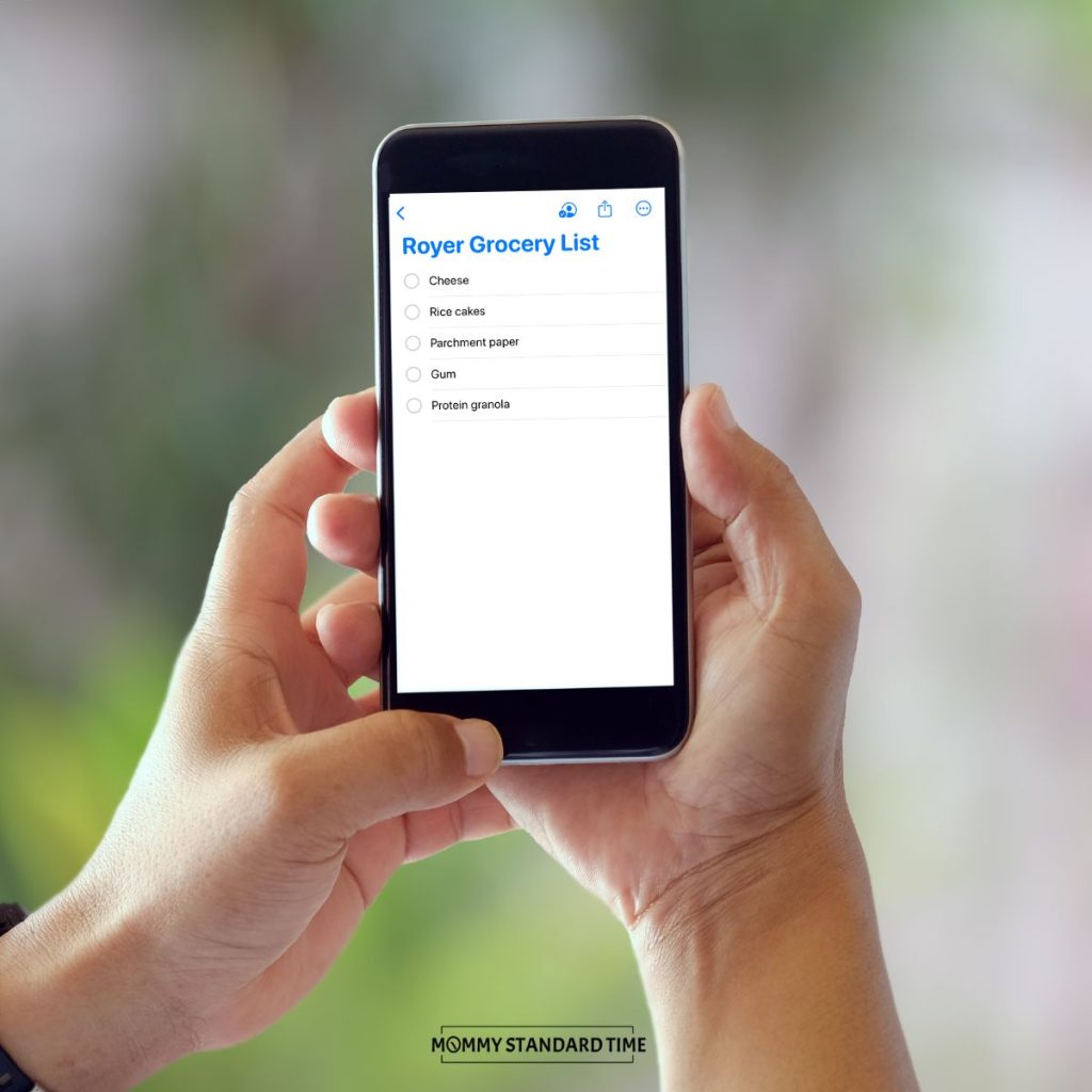 Two hands holding an iPhone displaying a family grocery list